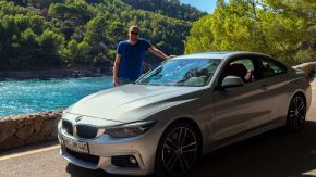 Robert hinter BMW 440i Coupé mit der Bucht von Cala Tuent im Hintergrund