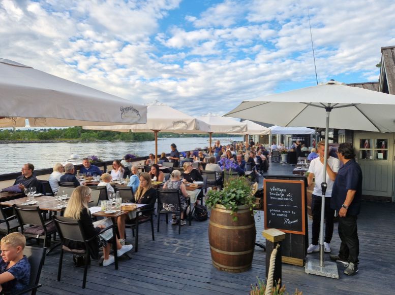 Menschen sitzen auf der Terrasse des Restaurants Rokeriet auf Fjöderholmen, Schweden